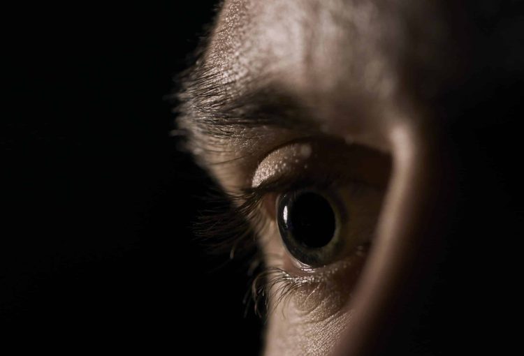 A closeup of a green human eye with dilated pupils on a black background